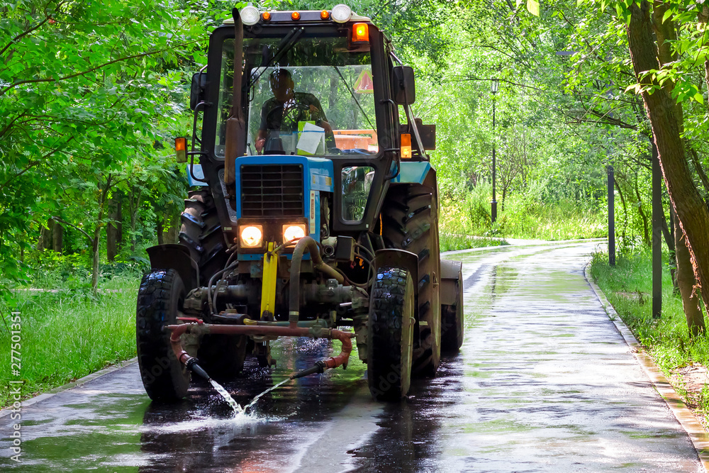 Tractor watering asphalt in the park. Worker cleans the asphalt washes the road in the park