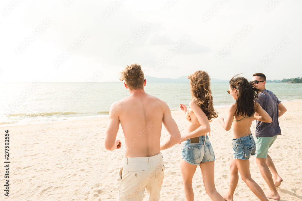 Group of young happy friends running from the beach to the sea
