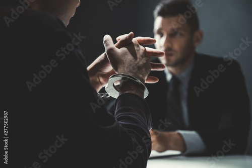 Criminal man with handcuffs being interviewed in interrogation room photo