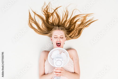 top view of girl yelling in Electric Fan and suffering from heat on white