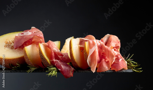 Prosciutto with melon and rosemary on a black background.