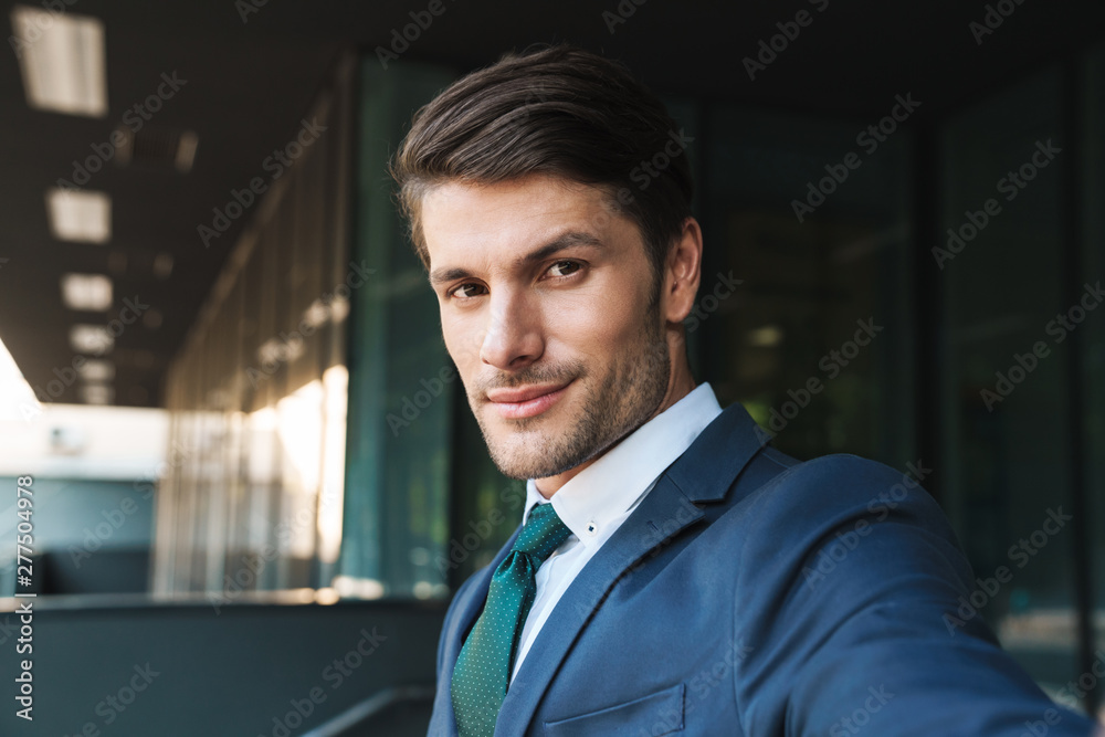 Obraz premium Photo of young businessman looking at camera and taking selfie while standing outside job center