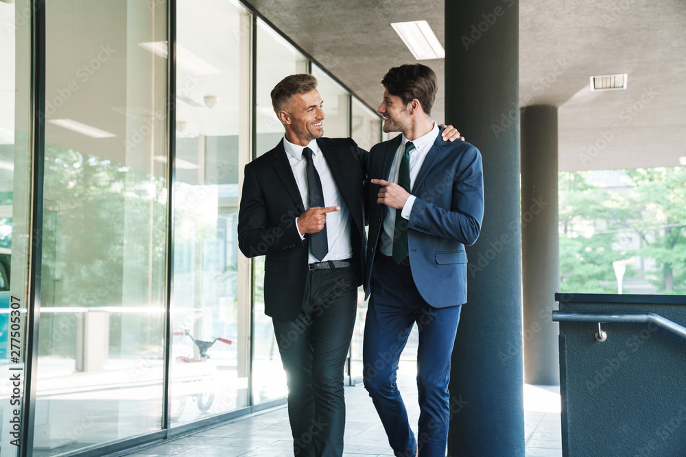 Portrait of two smiling businessmen partners walking outside job center during working meeting Portrait of two smiling businessmen partners walking outside job center during working meeting