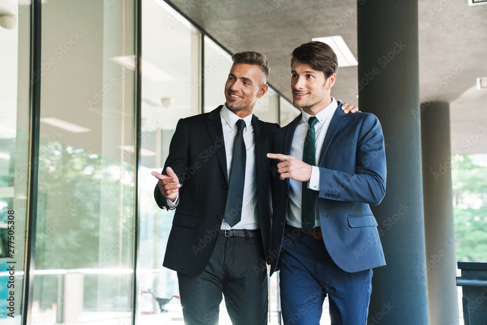 Portrait of two smiling businessmen partners walking outside job center during working meeting Portrait of two smiling businessmen partners walking outside job center during working meeting