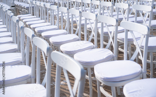 Rows of white chairs in rows on the beach sand. Conference or outdoor wedding. Watching a movie or a street theater.