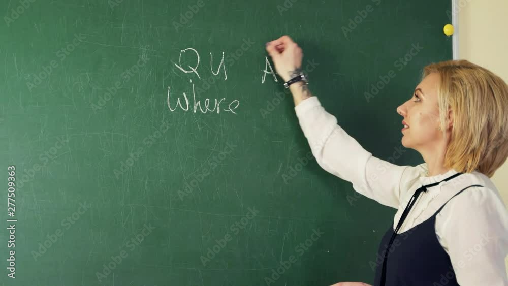 In an English class, a teacher writes with chalk on a blackboard and teaches students a lesson. In an English class, a teacher writes with chalk on a blackboard and teaches students a lesson.