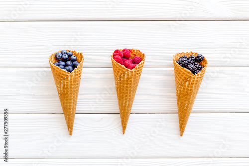 Fresh berries in waffle cones on white wooden background top view