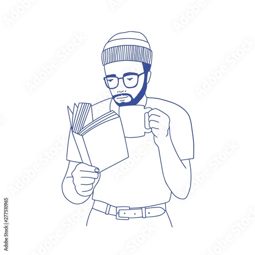 Pensive bearded man with glasses holding cup, drinking coffee and reading book