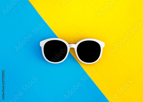 Sunny stylish white sunglasses on a bright blue-cyan and yellow-orange background, top view, isolated. Copy space. Flat lay
