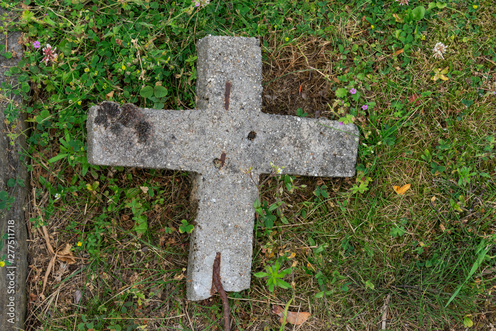 Old concrete cross that has fallen in the grass
