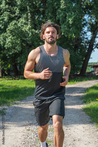 Young handsome man running on gravel road in nature vertical