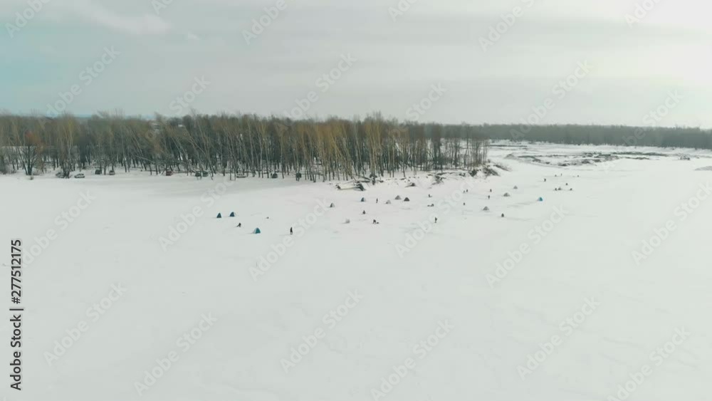 fishermen silhouettes settle on ice of frozen river surface covered with snow near thick pine tree forest aerial view fishermen silhouettes settle on ice of frozen river surface covered with snow near thick pine tree forest aerial view