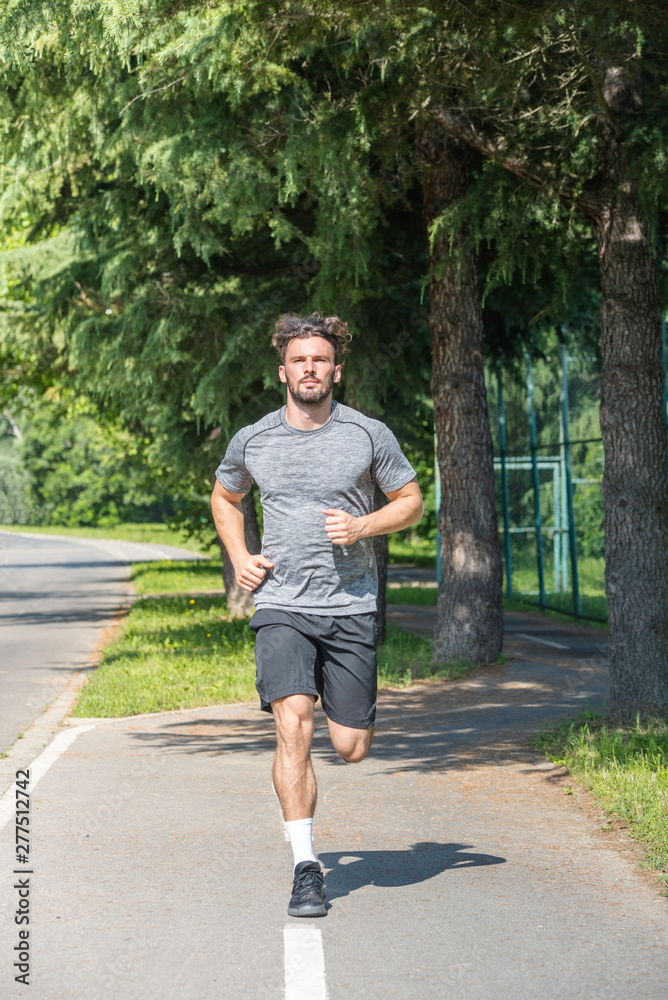 Handsome man running in park with trees in background vertical