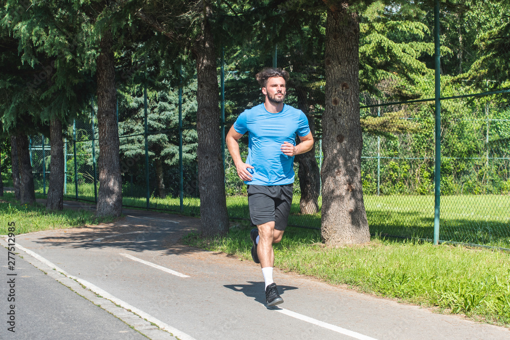 Fototapeta premium Handsome man running in park with trees in background