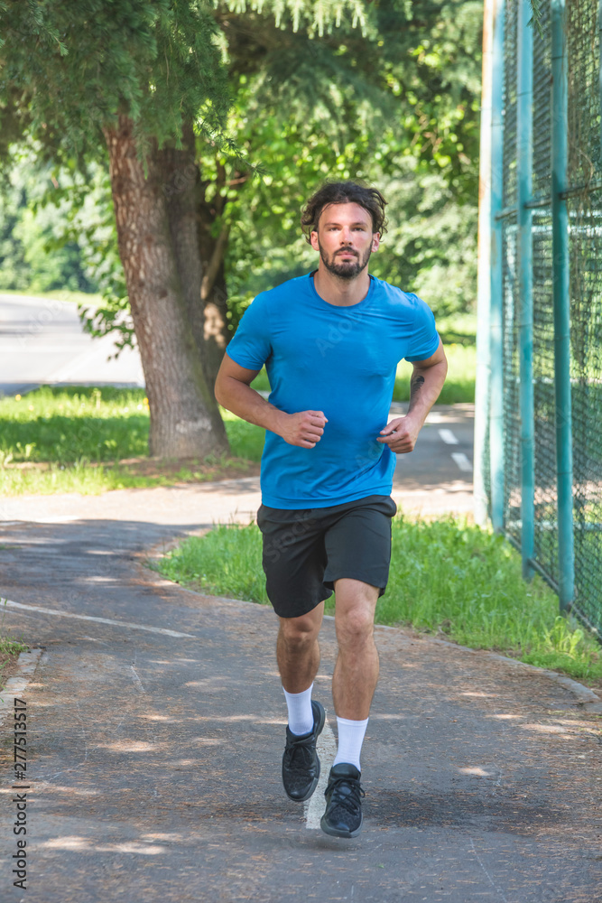 Handsome man running in park with trees in background Handsome man running in park with trees in background