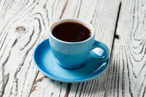 One full blue cup with saucer full of hot fresh black coffee on old rustic wooden table on kitchen