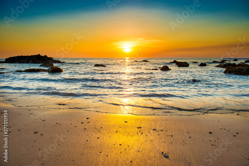 Beautiful colorful sunset landscape with sand beach, golden sun and stones at sea shore