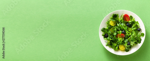 Fotografia, Obraz banner of fresh salad of arugula and valerian leaves with colored tomatoes and blueberries in a plate on a green background