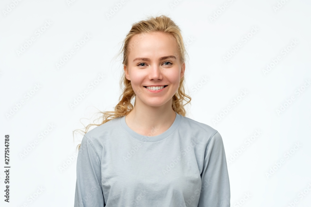 Headshot portrait of happy blonde girl in blue pulover smiling looking at camera. White background. Positive facial human emotion. Headshot portrait of happy blonde girl in blue pulover smiling looking at camera. White background. Positive facial human emotion.