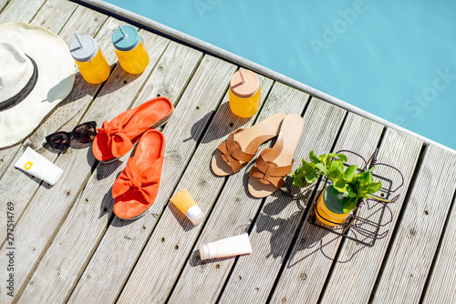 View on the poolside with accessories for summer vacations  drinks  slippers  sunglasses  sunscreen lotions and hat