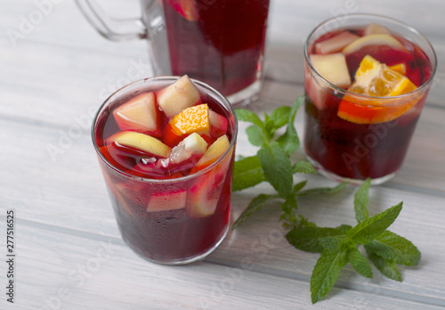 Two glasses with sangria next to jug and mint leaves, on wooden table. Typical Spanish drink with wine and fruits.