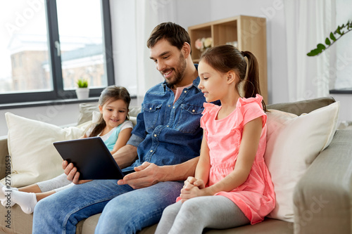 family, leisure and people concept - happy father and daughters with tablet pc computer at home