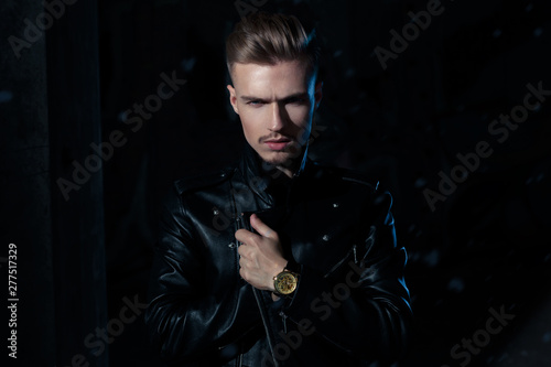 Low key dark fashionable caucasian man in leather jacket and black jeens with blue rim light. Vampire like concept