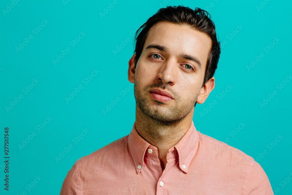 Portrait of a young man with head tilted, isolated on blue studio background