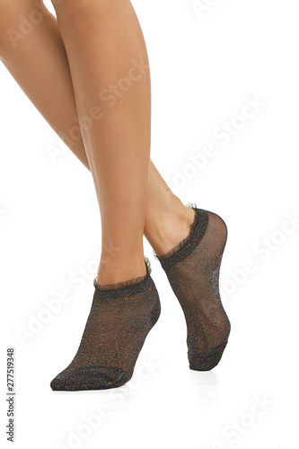 Cropped half-turn shot of lady's legs with smooth skin, wearing ink black low-cut socks with opalesce lurex, adorned with lace ruffles on elastic band. The woman is making step on white background.