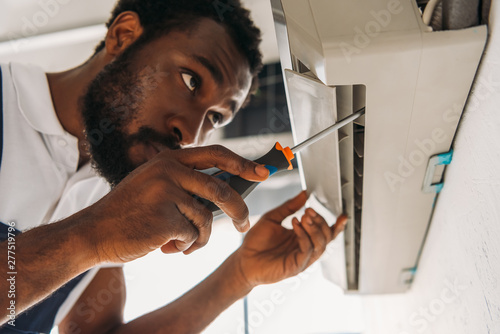serious african american repairman fixing air conditioner with screwdriver