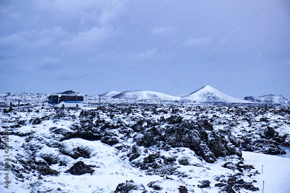 Fototapeta premium Keflavik - January 2019: Two Busses Standing On The Road In The Middle Of The Beautiful Icelandic Landscape With Snow Covered Mountains In The Area Of The Blue Lagoon