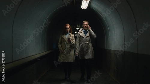 Zoom out shot of businessman talking on mobile phone going through the tunnel with redhead woman texting on smartphone in the evening photo