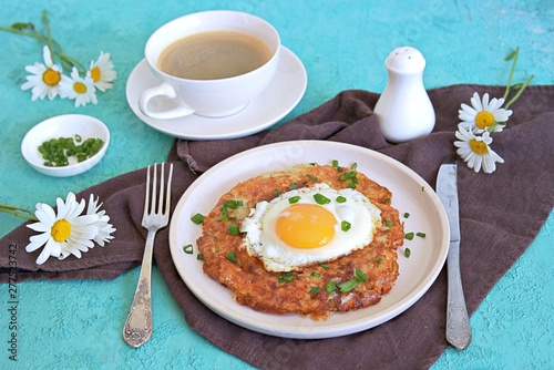 Rosti, fried potato pancake from boiled potatoes with egg on a white clay plate on a turquoise background. Swiss cuisine.