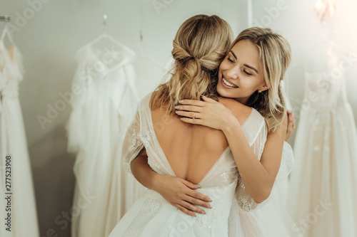 Two brides hugging each other in a wedding shop.
