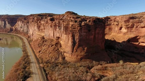 Flying next to brightly colored rock formations with surrounding sandstone rocks all seen from the air.  River flowing on one side and rock formations on the other side. photo