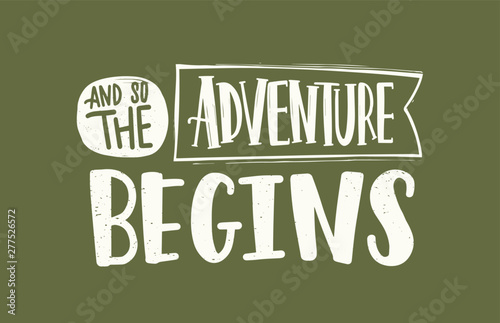 And So The Adventure Begins slogan, message or phrase written with elegant cursive calligraphic font on ribbon