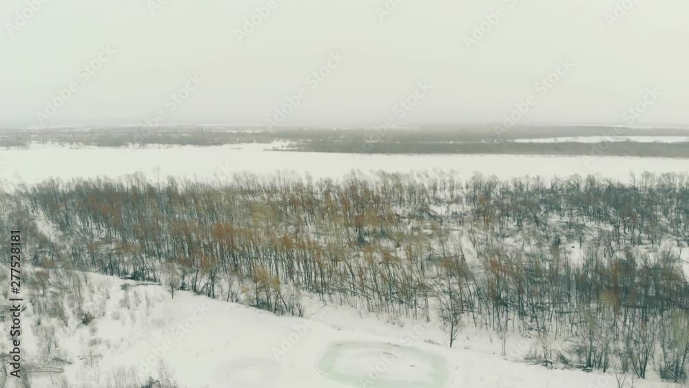 snowy mountain slope at melancholic bare forest against wide frozen river under grey sky aerial view snowy mountain slope at melancholic bare forest against wide frozen river under grey sky aerial view