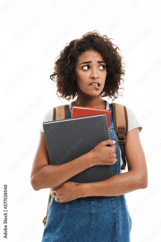 Image of anxious african american woman wearing backpack frowning and holding exercise books Image of anxious african american woman wearing backpack frowning and holding exercise books