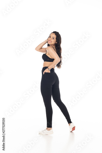 full length view of smiling sexy girl in black bra and pants with hand in pocket isolated on white