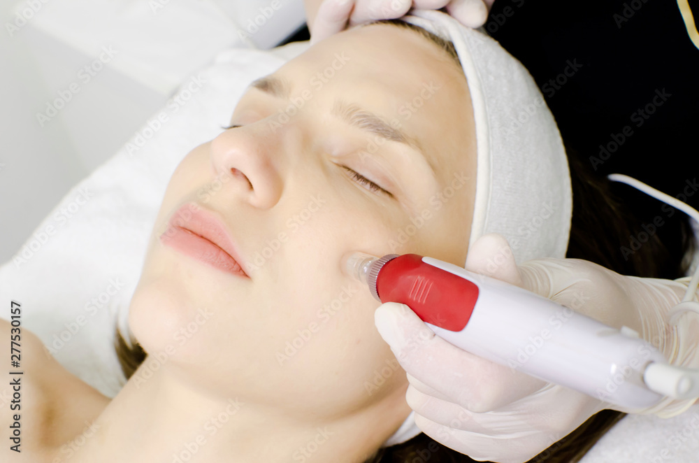 Cosmetologist,beautician in white gloves applying facial dermapen treatment on face of young girl customer in beauty salon.Cosmetology and professional skin care