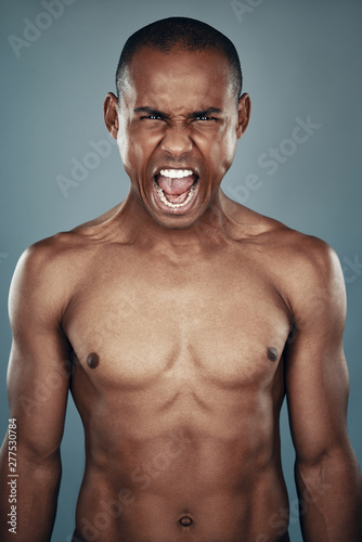 Furious man. Shirtless young African man looking at camera and shouting while standing against grey background