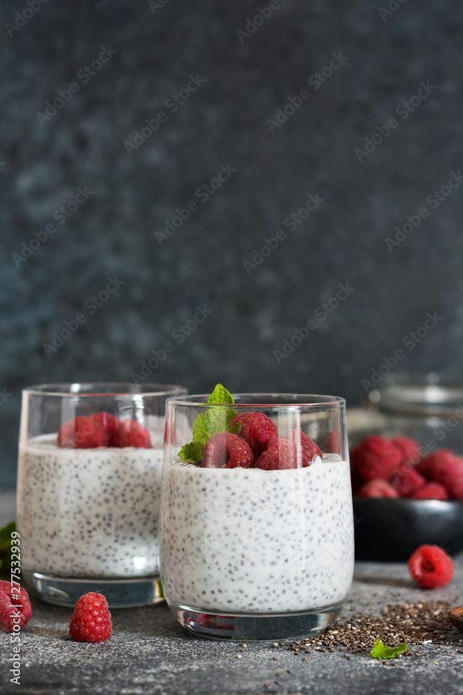 Chia pudding with yogurt and raspberries in a glass on concrete background Chia pudding with yogurt and raspberries in a glass on concrete background