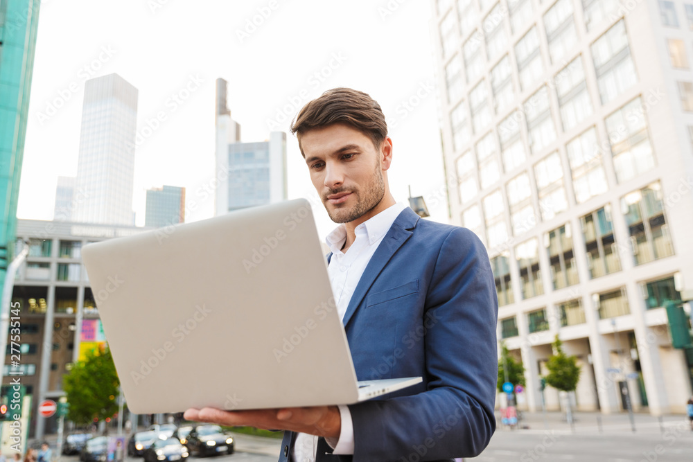 Serious concentrated handsome young business man standing near business center using laptop computer. Serious concentrated handsome young business man standing near business center using laptop computer.