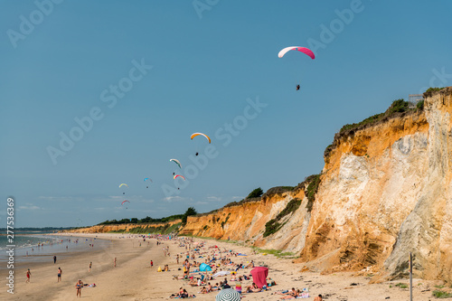 parachutes over a sandy beach on a steep coast