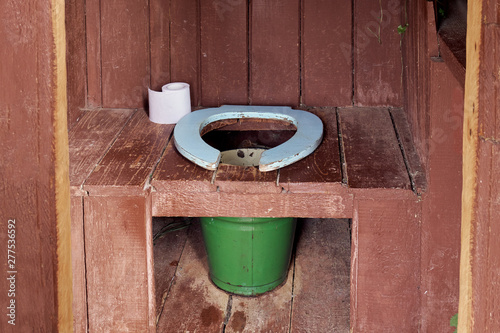 Interior of a country wooden outdoor toilet with a metal bucket as a waste tank and a roll of a paper photo