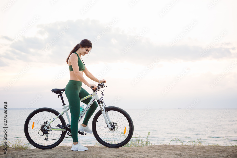 Young brunette woman on a bicycle at sunrise.