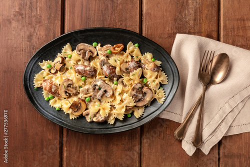 Mushroom and cheese pasta. Farfalle with cremini and green peas, shot from the top on a dark rustic wooden background with a place for text