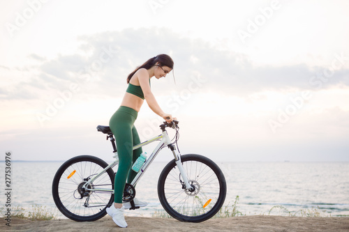 Young brunette woman on a bicycle at sunrise.