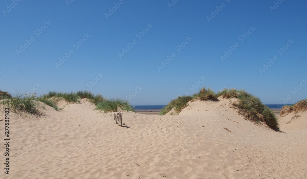 grass covered sand dunes with a small wooden fence against a blue summer sky in formby on the merseyside coast