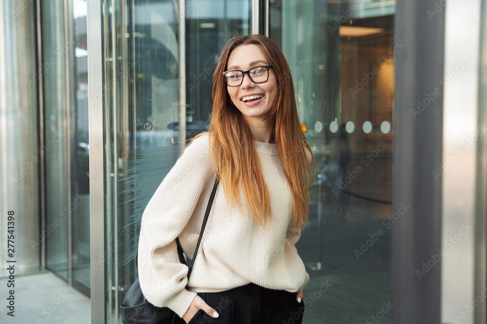 Beautiful young business woman posing walking outdoors near business center wearing eyeglasses